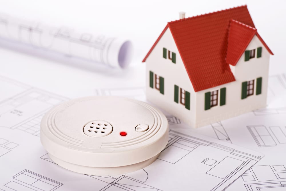 Smoke detector and model house on architectural blueprints.